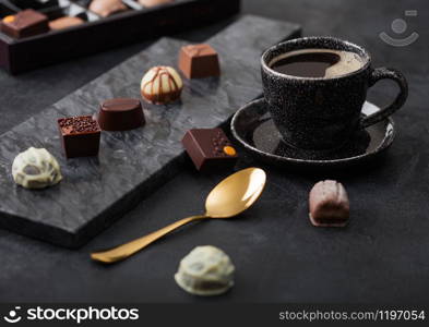 Luxury Chocolate candies selection with cup of black coffee and golden spoon on black marble board and dark background.