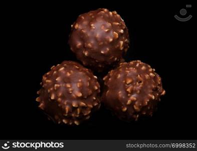 Luxury chocolate candies with hazelnuts and cocoa cream on black.