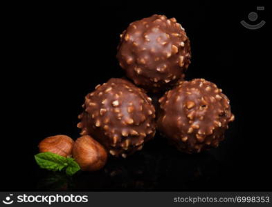 Luxury chocolate candies with hazelnuts pieces and mint leaf on black marble background.