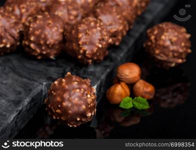 Luxury chocolate candies with hazelnuts pieces and mint leaf on black marble background.