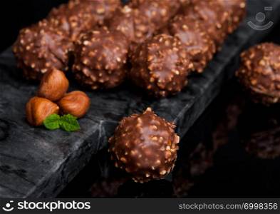 Luxury chocolate candies with hazelnuts pieces and mint leaf on black marble background.