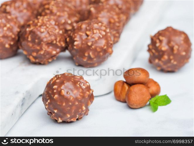Luxury chocolate candies with hazelnuts pieces and mint leaf on marble background.