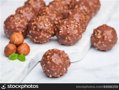 Luxury chocolate candies with hazelnuts pieces and mint leaf on marble background.