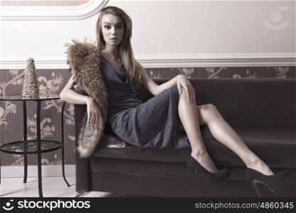 luxury fashion portrait in elegant ambient of stunning woman with long hair, make-up, blue elegant shiny dress and fur on shoulder. In charming pose is looking in camera