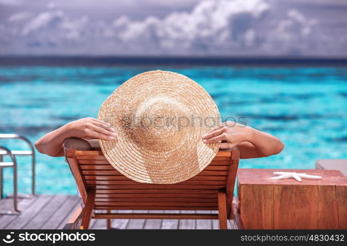 Luxury female tanning on the beach, wearing big stylish hat, enjoying beautiful seascape, summer travel and tourism concept