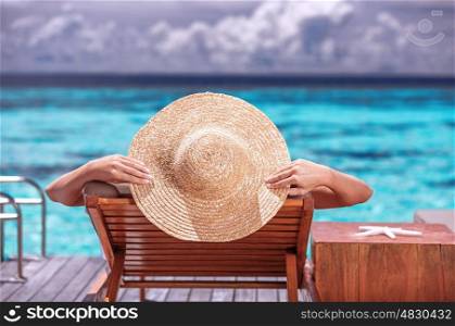 Luxury female tanning on the beach, wearing big stylish hat, enjoying beautiful seascape, summer travel and tourism concept