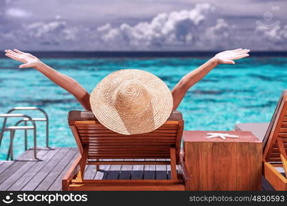 Luxury female tanning on the beach, wearing big stylish hat, enjoying beautiful seascape, summer fashion, travel and tourism concept