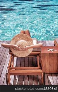 Luxury female tanning on the beach, wearing big stylish hat, enjoying beautiful seascape, summer travel and tourism concept