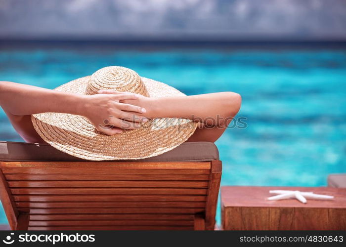 Luxury female tanning on the beach, wearing big stylish hat, enjoying beautiful seascape, summer fashion, travel and tourism concept