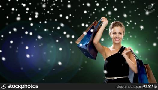 luxury, holydays, people and sale concept - smiling woman with shopping bags over snow and night lights background