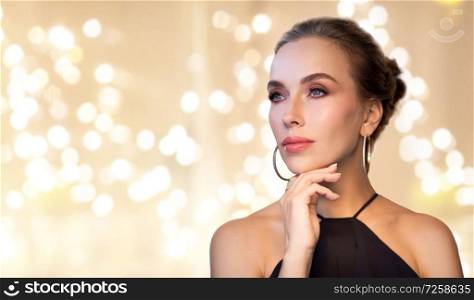 luxury, jewelry and people concept - beautiful woman in black wearing diamond earring and ring over beige background and festive lights. beautiful woman in black wearing diamond jewelry