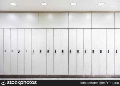 Luxury lookers in a row, in artificial light. White metal wardrobes. Cloakroom with white lockers. Back to school context. Dressing room interior.
