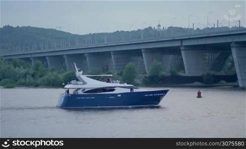 Luxury private motor yacht sailing on river near bridge over postindustrial cityscape