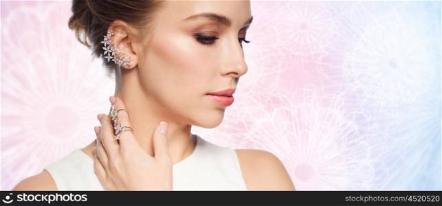 luxury, wedding and people concept - smiling woman in white dress with diamond jewelry over rose quartz and serenity patterned background (focus on earring and ring on finger)