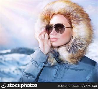 Luxury woman portrait in wintertime, wearing stylish sunglasses and warm coat with furry hood and looking away, winter fashion concept&#xA;