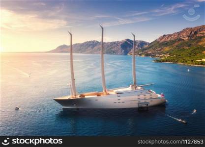 Luxury yacht and blue sea at colorful sunset in summer. Aerial view of big modern sail boat. Top view of beautiful futuristic yacht, lagoon, boats, mountains, clear water, sky. Travel in Adriatic sea