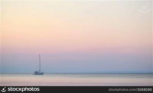 Luxury yacht moored offshore at sunset on a tranquil ocean under a delicate pink coloured sky