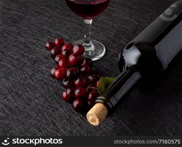 Lying bottle of wine and red grape on a dark background. Bottle of wine and dark grapes on a dark background