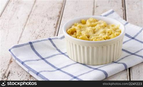 Mac and Cheese, macaroni pasta with cheese in ceramic bowl on napkin on white old wood texture background