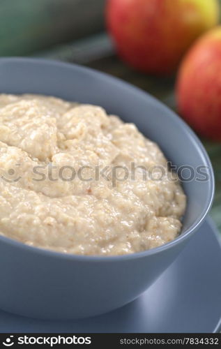 Maca-Oatmeal Porridge. Bowl of cooked oatmeal porridge mixed with powdered maca or Peruvian ginseng (lat. Lepidium meyenii) with apples in the back (Selective Focus, Focus in the middle of the porridge)