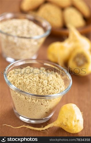 Maca powder (flour) in glass bowl with maca roots or Peruvian ginseng (lat. Lepidium meyenii) and other Peruvian maca products (oatmeal with maca and maca cookies) in the back (Selective Focus, Focus one third into the maca powder and on the front of the maca root beside the bowl). Maca Root and Maca Powder (Flour)