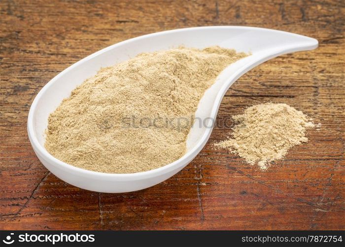 maca root powder in a teardrop shaped bowl against grunge wood