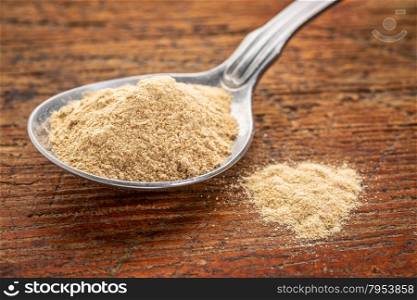 maca root powder on a tablespoon against rustic wood - superfood supplement concept