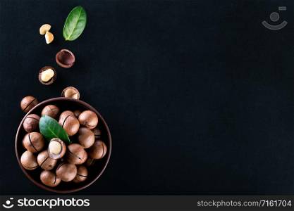 Macadamia nuts in a clay plate with grains and leaves on a black background. View from above