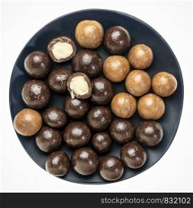 macadamia nuts in shells and dipped in dark chocolate on a black plate isolated on white