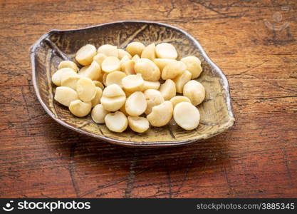 macadamia nuts on a ceramic leafs shaped bowl against rustic wood