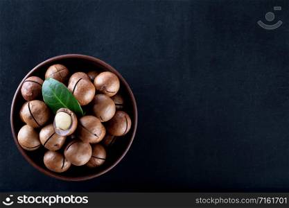 Macadamia nuts with a leaf in a clay plate on a black background. View from above. Macadamia nuts in clay plate on black background