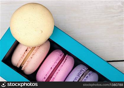 Macaroons in box and one on top on wooden background. Macaroons in box and one on top