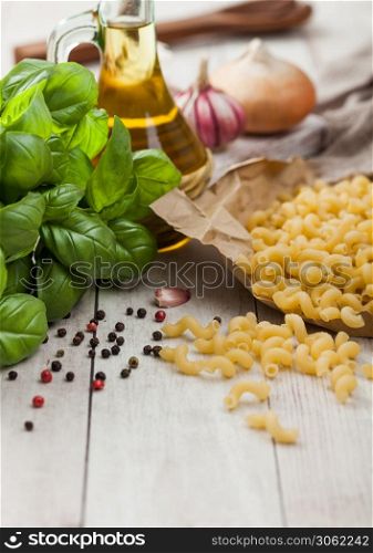 Maccheroni elbows classic raw pasta in brown paper on light wooden table background with basil and oil, pepper and onion.