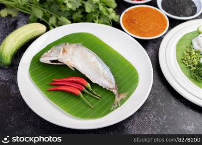 Mackerel paste and chilies on banana leaves on a white plate, complete with liquid and vegetables.