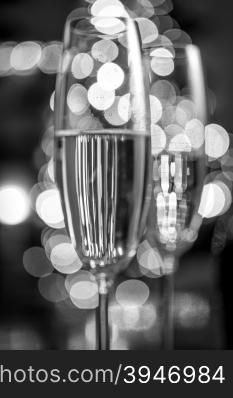 Macro black and white photo of two champagne glasses on background of Christmas lights