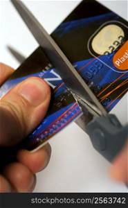 Macro image of scissors cutting through a credit card. Logos are fake and numbers have been changed. Colours of the card have been altered also.