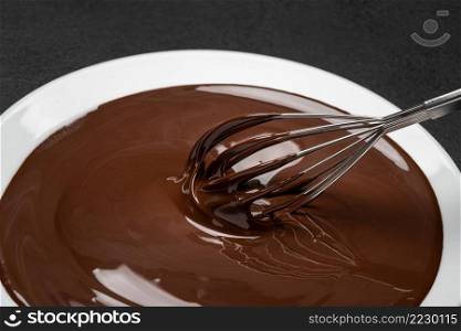 Macro of Melted milk or dark chocolate swirl in plate and whisk on dark concrete background. Macro of Melted milk or dark chocolate swirl in plate and whisk on concrete background