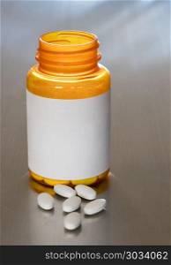 Macro of white tablets on metal table. Prescription bottle with blank label for copy space and white pills or tablets on metal table for opioid epidemic illustration. Macro of white tablets on metal table
