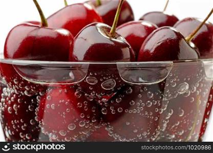 Macro photo of fresh and natural red cherries in a glass with water and bubbles