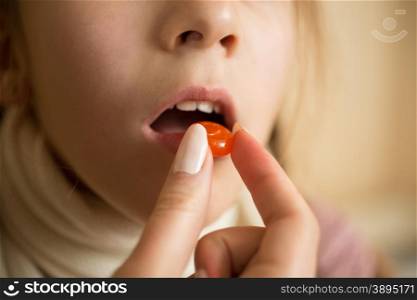 Macro photo of little sick with flu girl taking pill in mouth