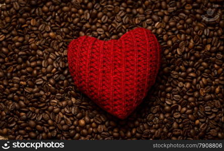 Macro photo of red knitted heart lying on coffee beans