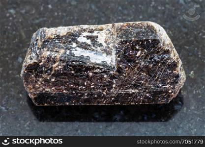 macro shooting of natural mineral rock specimen - brown crystal of dravite tourmaline gemstone on dark granite background from China