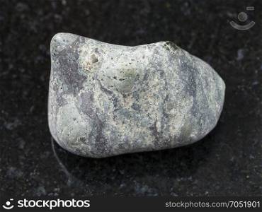 macro shooting of natural mineral rock specimen - pebble of Suevite stone on dark granite background from Karelia, Rissia