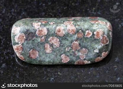 macro shooting of natural mineral rock specimen - polished Eclogite gemstone on dark granite background from Salma region, Kola peninsula, Russia