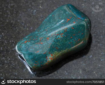 macro shooting of natural mineral rock specimen - polished green Heliotrope (bloodstone) gem stone on dark granite background from India