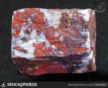 macro shooting of natural mineral rock specimen - raw Jasper stone on dark granite background from South Ural Mountains, Russia