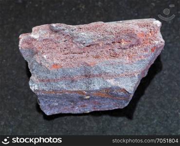 macro shooting of natural mineral rock specimen - raw jaspilite (ferruginous quartzite) stone on dark granite background