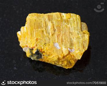 macro shooting of natural mineral rock specimen - raw native orpiment stone on dark granite background from Yakutia, Russia