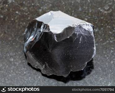 macro shooting of natural mineral rock specimen - raw obsidian (volcanic glass) crystal on dark granite background