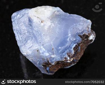 macro shooting of natural mineral rock specimen - rough crystal of blue Chalcedony gemstone on dark granite background from Transbaikalia (Zabaykalye), Russia